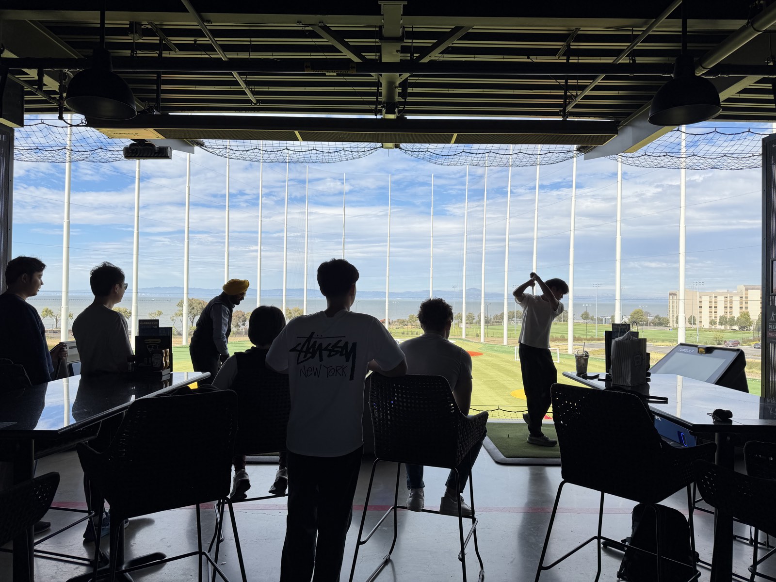 The Ember team watching a teammate swing at a Topgolf outing overlooking the bay